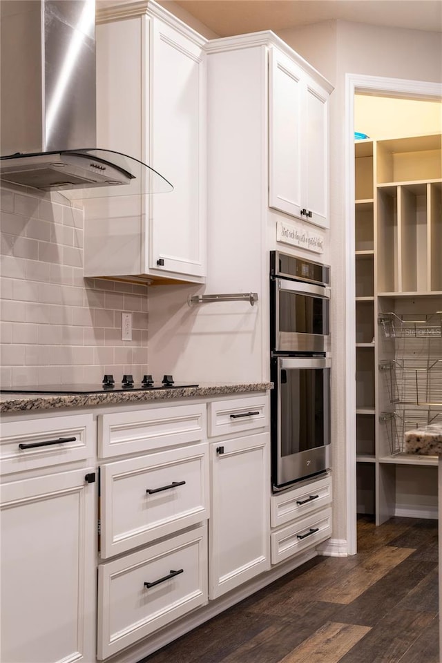 kitchen with white cabinets, dark hardwood / wood-style flooring, stainless steel double oven, and wall chimney range hood