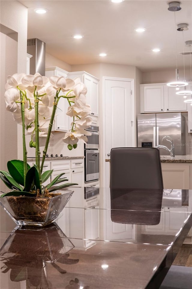 kitchen featuring stainless steel fridge with ice dispenser, white cabinetry, light stone counters, and decorative light fixtures