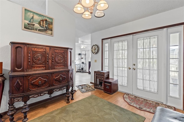 entrance foyer featuring french doors, ceiling fan with notable chandelier, vaulted ceiling, light hardwood / wood-style flooring, and a textured ceiling