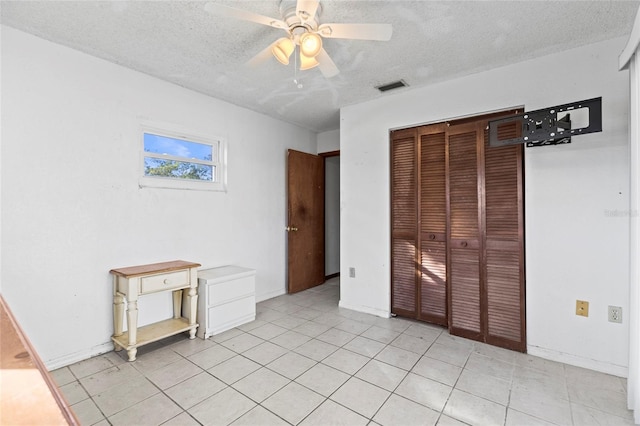 unfurnished bedroom with a textured ceiling, a closet, ceiling fan, and light tile patterned flooring