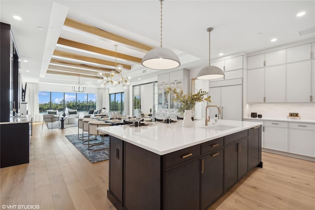 kitchen with white cabinets, sink, light wood-type flooring, tasteful backsplash, and decorative light fixtures