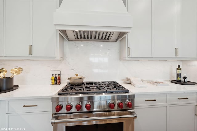 kitchen featuring custom exhaust hood, high end range, light stone countertops, tasteful backsplash, and white cabinetry