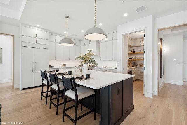 kitchen featuring paneled refrigerator, pendant lighting, light hardwood / wood-style floors, a kitchen island with sink, and white cabinets