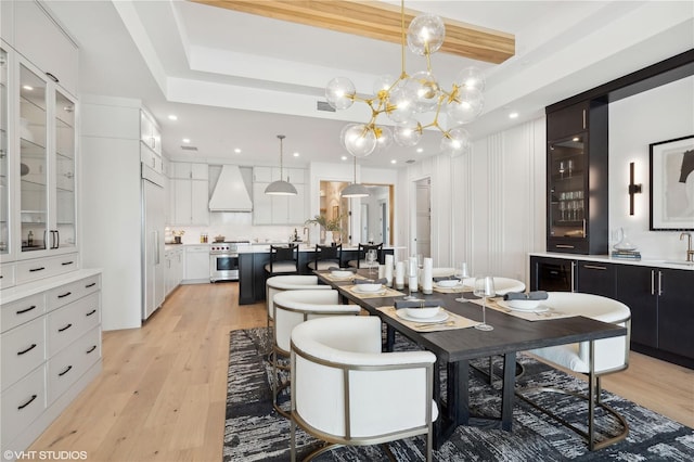 dining room with wine cooler, an inviting chandelier, a tray ceiling, and light hardwood / wood-style flooring