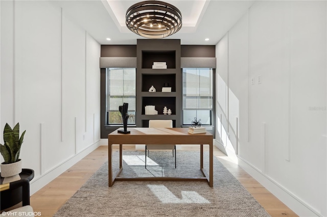 office space featuring a raised ceiling, plenty of natural light, and light hardwood / wood-style floors