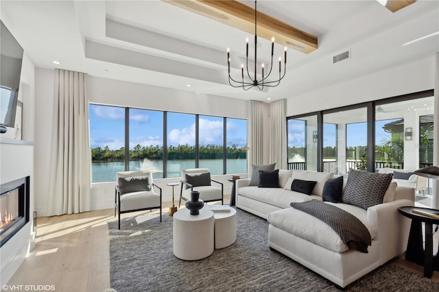 living room featuring a tray ceiling, hardwood / wood-style floors, a water view, and a chandelier