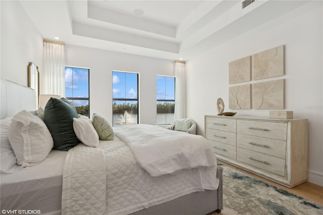 bedroom featuring hardwood / wood-style flooring, a raised ceiling, and multiple windows