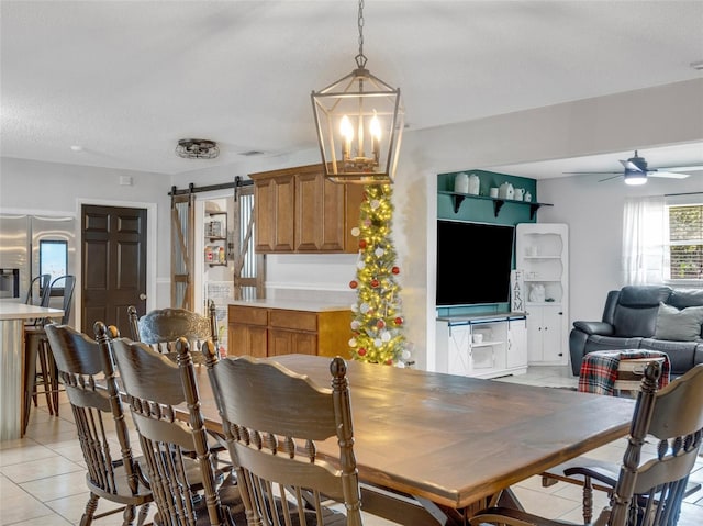 tiled dining area featuring ceiling fan with notable chandelier, a textured ceiling, and a barn door