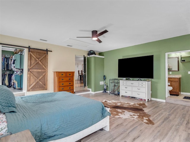 bedroom with ensuite bath, ceiling fan, a barn door, light wood-type flooring, and a closet