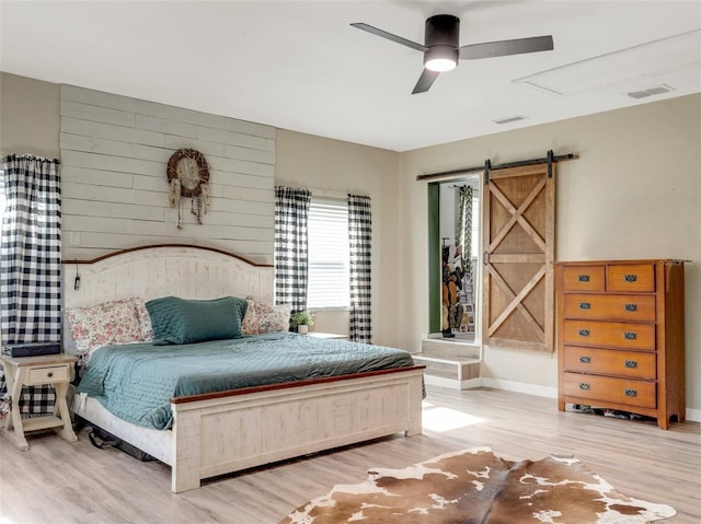 bedroom featuring wood finished floors, visible vents, baseboards, and a barn door