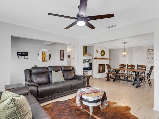 living area featuring a ceiling fan, a brick fireplace, visible vents, and light tile patterned flooring