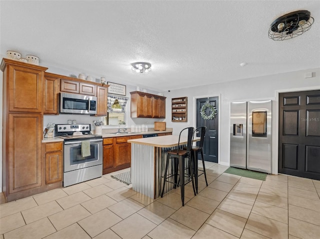 kitchen featuring a breakfast bar area, stainless steel appliances, light countertops, brown cabinetry, and a kitchen island