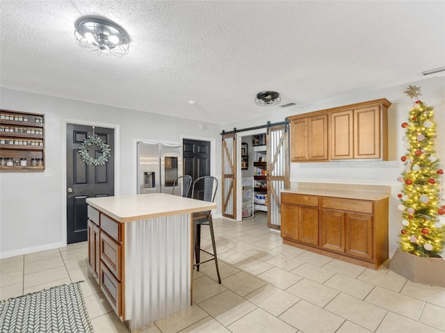 kitchen with a barn door, stainless steel fridge, a kitchen island, a breakfast bar, and light countertops