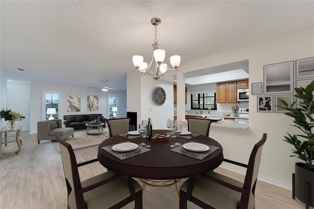 dining area featuring ceiling fan with notable chandelier, a textured ceiling, a wealth of natural light, and light hardwood / wood-style flooring