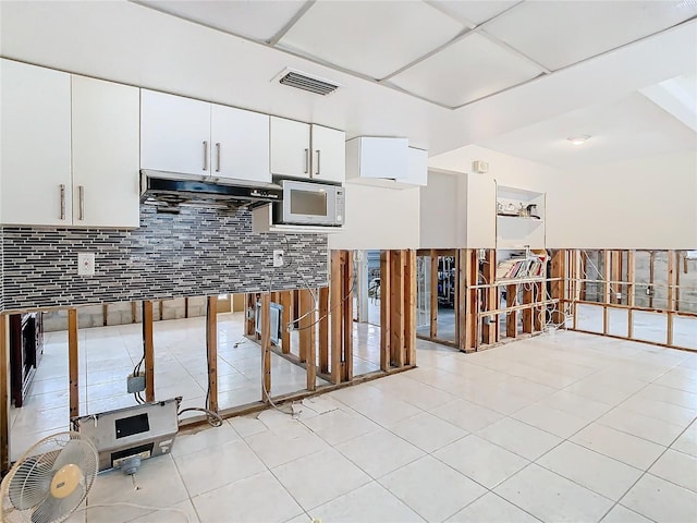 kitchen with a drop ceiling, light tile patterned flooring, white cabinetry, and backsplash