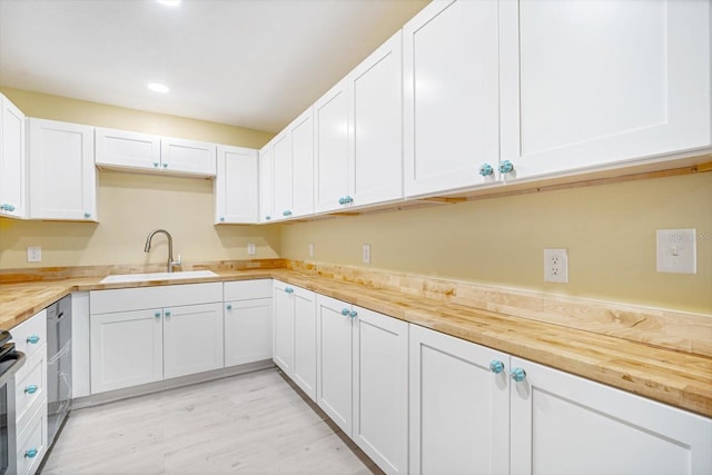 kitchen with butcher block counters, white cabinetry, sink, and light wood-type flooring