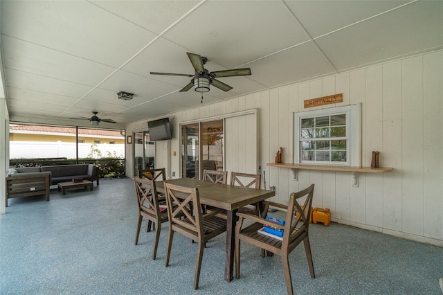 dining area featuring ceiling fan, a drop ceiling, and wooden walls