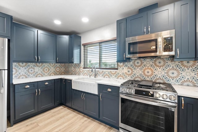 kitchen featuring sink, tasteful backsplash, light hardwood / wood-style flooring, blue cabinets, and appliances with stainless steel finishes