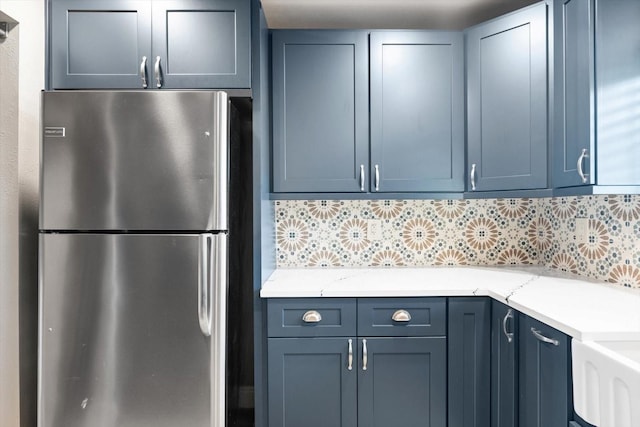 kitchen featuring light stone countertops, tasteful backsplash, stainless steel refrigerator, and blue cabinetry