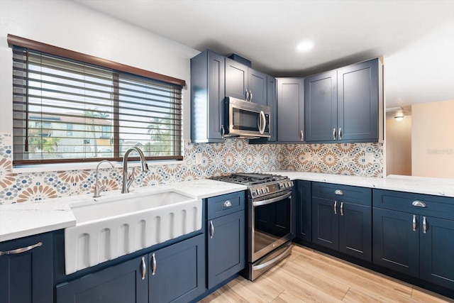 kitchen featuring light stone countertops, appliances with stainless steel finishes, light wood-type flooring, tasteful backsplash, and sink