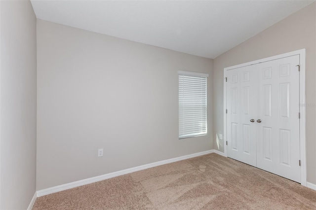 carpeted empty room featuring baseboards and vaulted ceiling