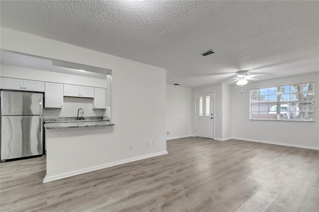 kitchen with stainless steel refrigerator, sink, light stone counters, white cabinets, and light wood-type flooring