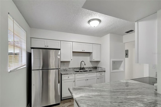 kitchen featuring sink, stainless steel fridge, a textured ceiling, light stone counters, and white cabinetry