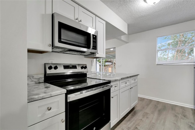 kitchen featuring a wealth of natural light, white cabinetry, stainless steel appliances, and light stone counters