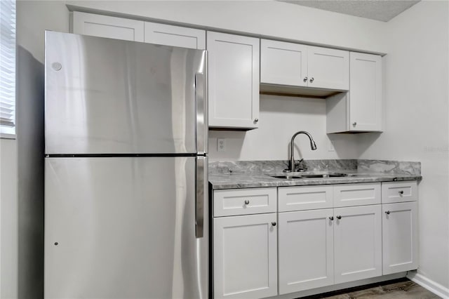 kitchen featuring white cabinetry, stainless steel fridge, sink, and light stone counters