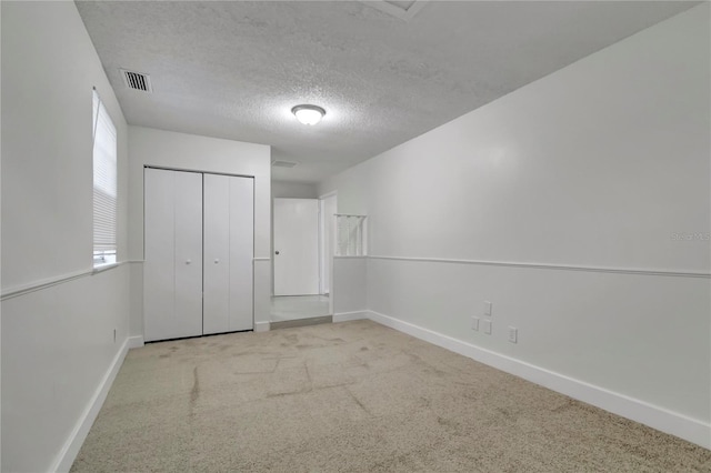 unfurnished bedroom featuring a textured ceiling, light carpet, and a closet