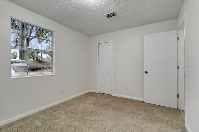 unfurnished bedroom with light carpet, a textured ceiling, and a closet