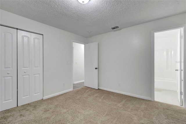 unfurnished bedroom with light carpet, a textured ceiling, connected bathroom, and a closet