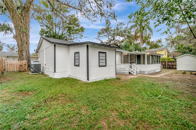 back of house with central air condition unit, a sunroom, and a yard