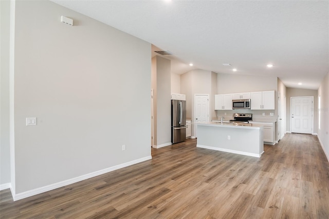 kitchen featuring appliances with stainless steel finishes, white cabinets, vaulted ceiling, and wood finished floors