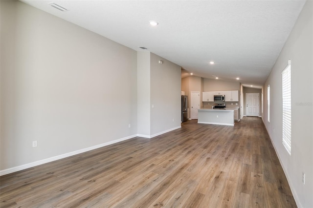 unfurnished living room with recessed lighting, visible vents, vaulted ceiling, wood finished floors, and baseboards