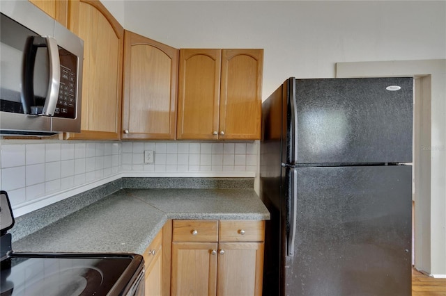 kitchen featuring decorative backsplash, black refrigerator, and range with electric stovetop