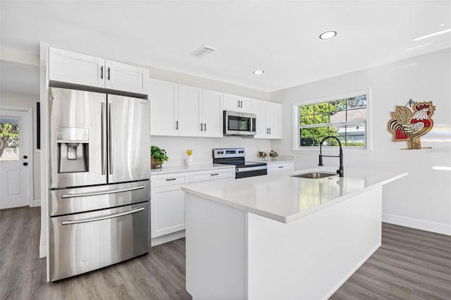 kitchen featuring appliances with stainless steel finishes, sink, hardwood / wood-style flooring, white cabinetry, and an island with sink