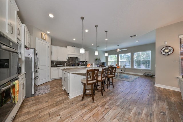 13230 Fawn Lily Dr, Riverview, FL 33579 - kitchen with stainless steel appliances, light wood finished floors, a ceiling fan, decorative backsplash, and white cabinets