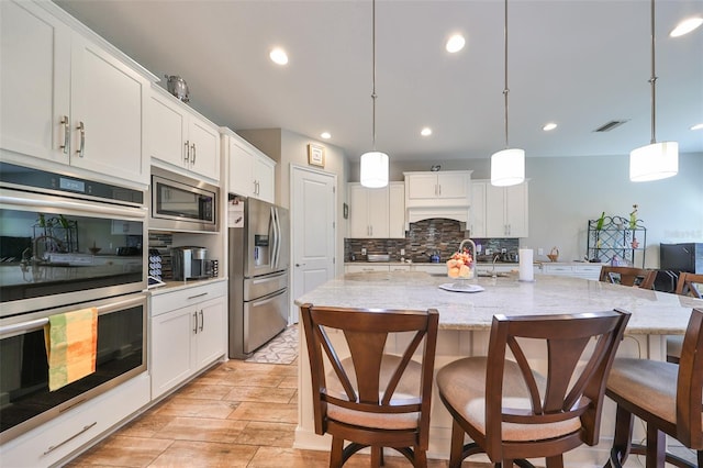 kitchen with a center island with sink, decorative light fixtures, white cabinets, and stainless steel appliances