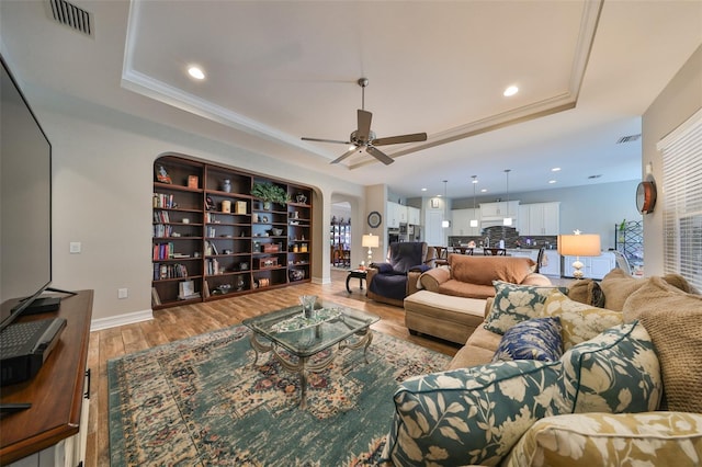 living room featuring ceiling fan, crown molding, a tray ceiling, and light hardwood / wood-style flooring