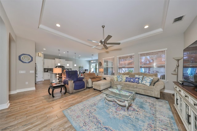 living room with ceiling fan, ornamental molding, a tray ceiling, and light hardwood / wood-style flooring