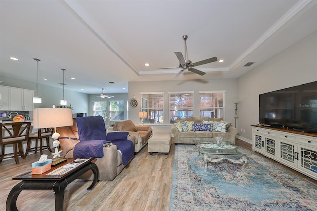 living room with ceiling fan, light hardwood / wood-style floors, a raised ceiling, and crown molding