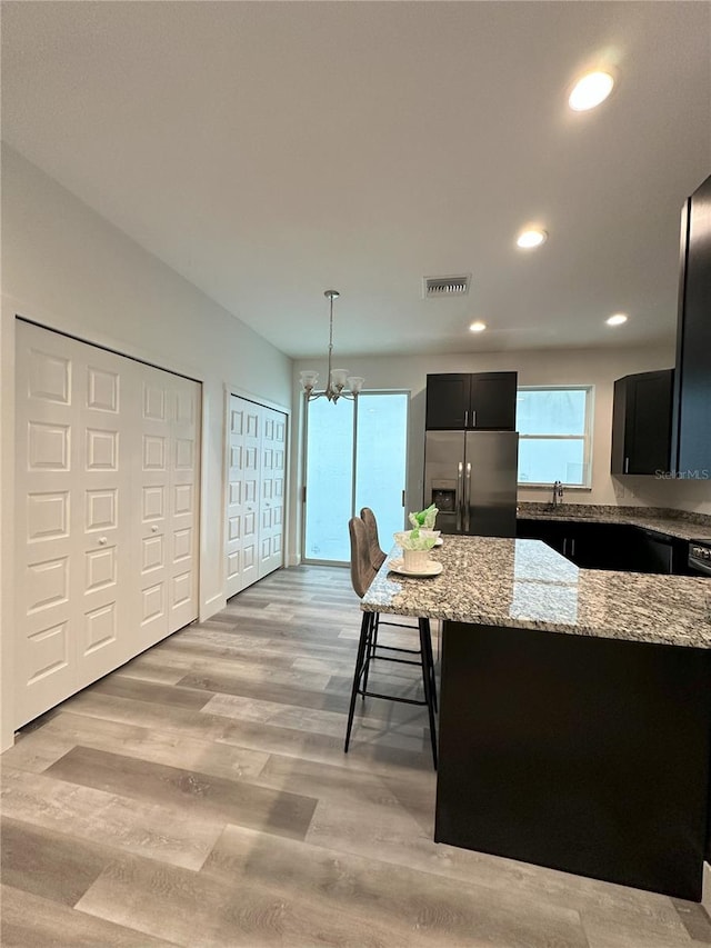 3208 Deleuil Ave, Tampa, FL 33610 - kitchen with stainless steel refrigerator with ice dispenser, light stone counters, dark cabinets, a chandelier, and light wood-style floors
