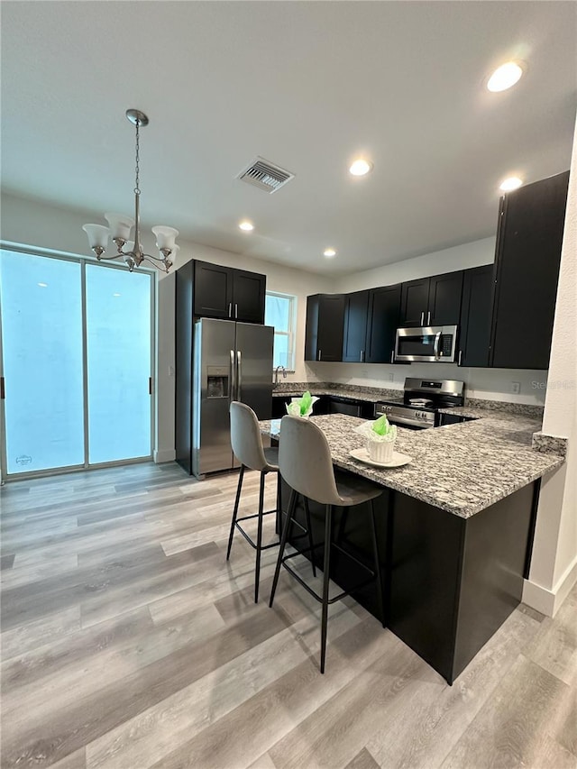 kitchen featuring appliances with stainless steel finishes, light hardwood / wood-style flooring, a kitchen breakfast bar, and a notable chandelier