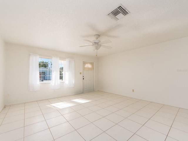 tiled empty room with ceiling fan and a textured ceiling