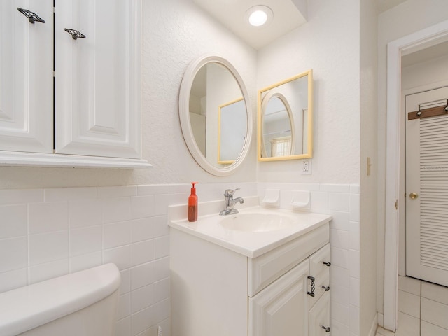 bathroom featuring toilet, vanity, and tile walls