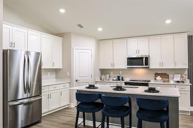 kitchen featuring vaulted ceiling, a center island with sink, white cabinetry, a kitchen breakfast bar, and stainless steel appliances