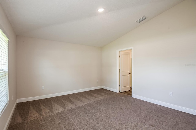 spare room with lofted ceiling, dark carpet, visible vents, and baseboards