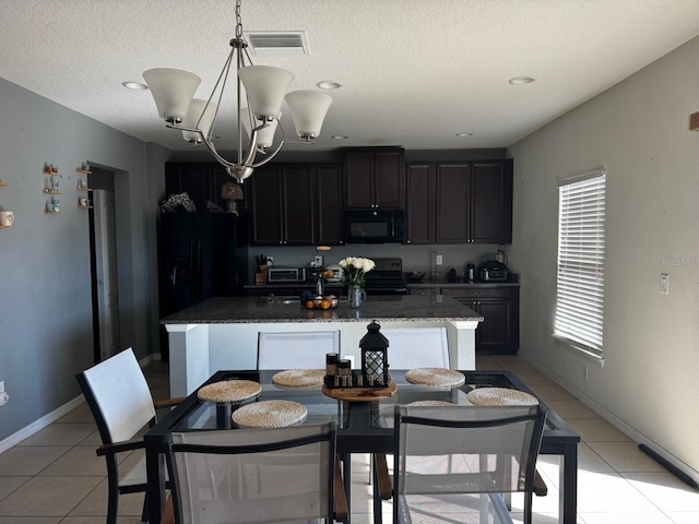 kitchen featuring dark stone countertops, pendant lighting, a kitchen island with sink, light tile patterned floors, and black appliances