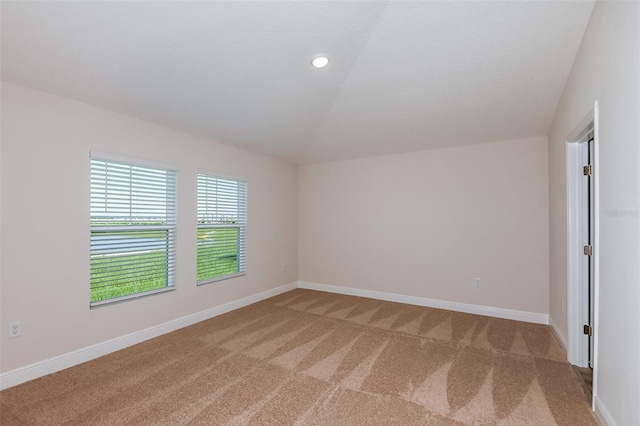 spare room featuring recessed lighting, light carpet, vaulted ceiling, and baseboards